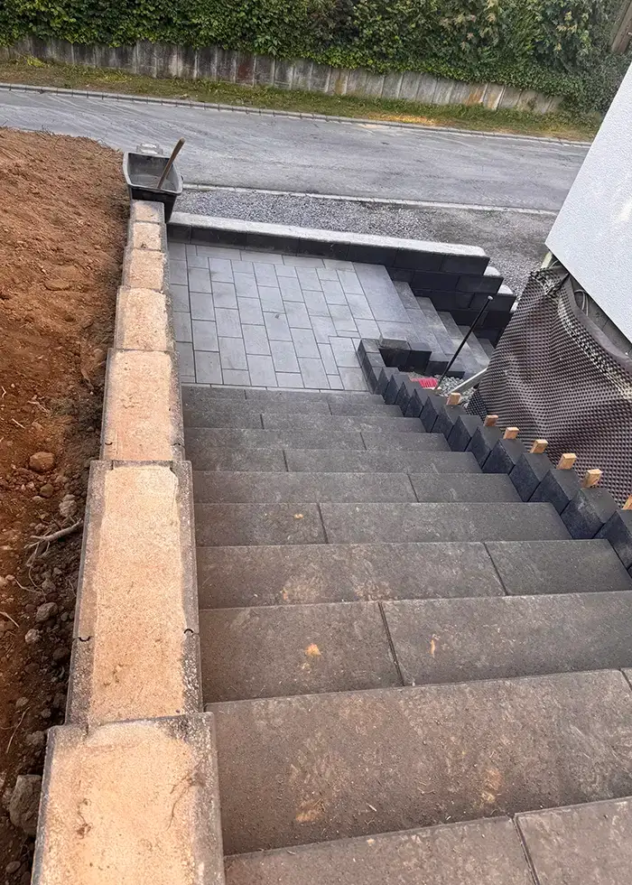 Neue Treppenanlage mit grauen Betonstufen und angrenzender gepflasterter Fläche vor einem Wohnhaus in einer ruhigen Wohnstraße