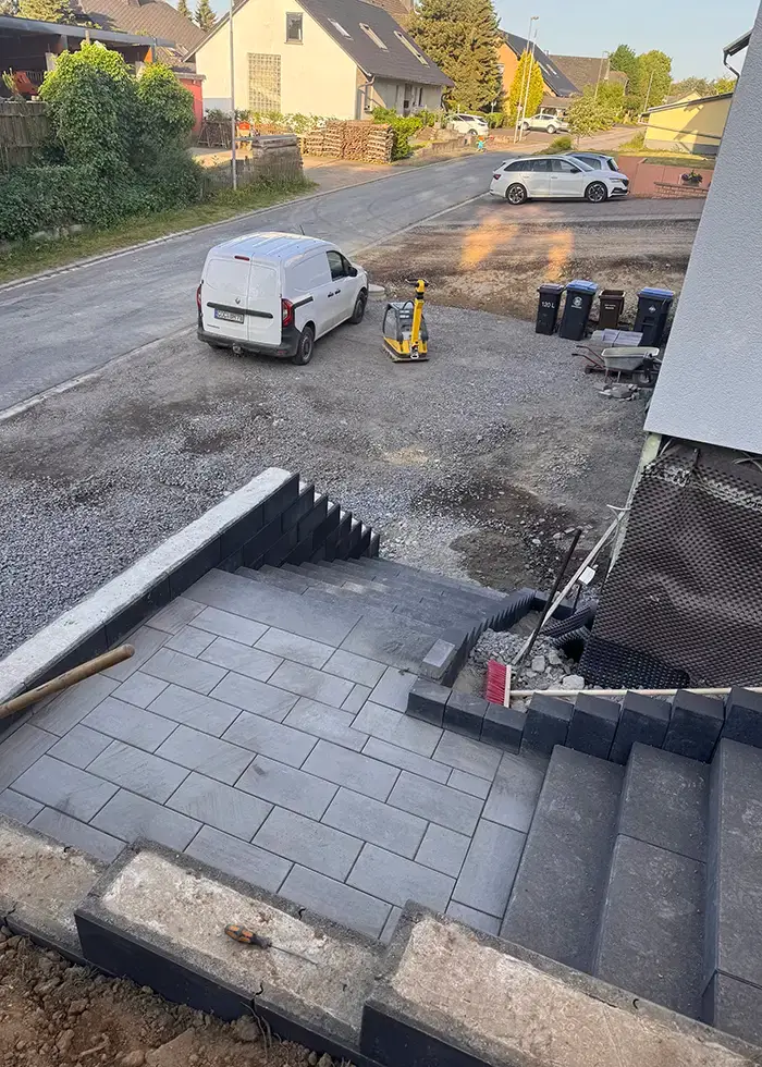 Neue Treppenanlage mit grauen Betonstufen und angrenzender gepflasterter Fläche vor einem Wohnhaus in einer ruhigen Wohnstraße
