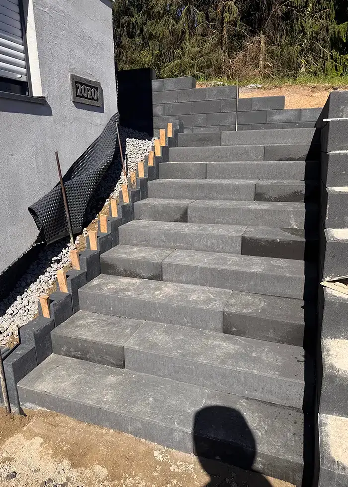 Außenanlage mit breiter Treppe aus grauen Betonstufen neben einem Haus