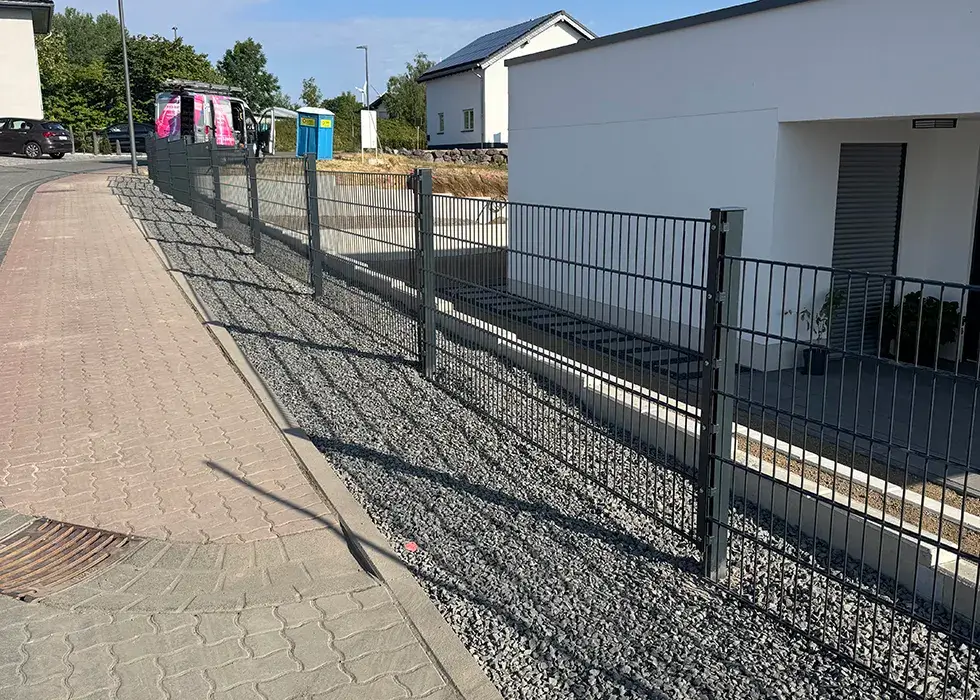 Metallzaun mit senkrechten und waagerechten Stäben entlang eines Gehwegs und eines Hauses